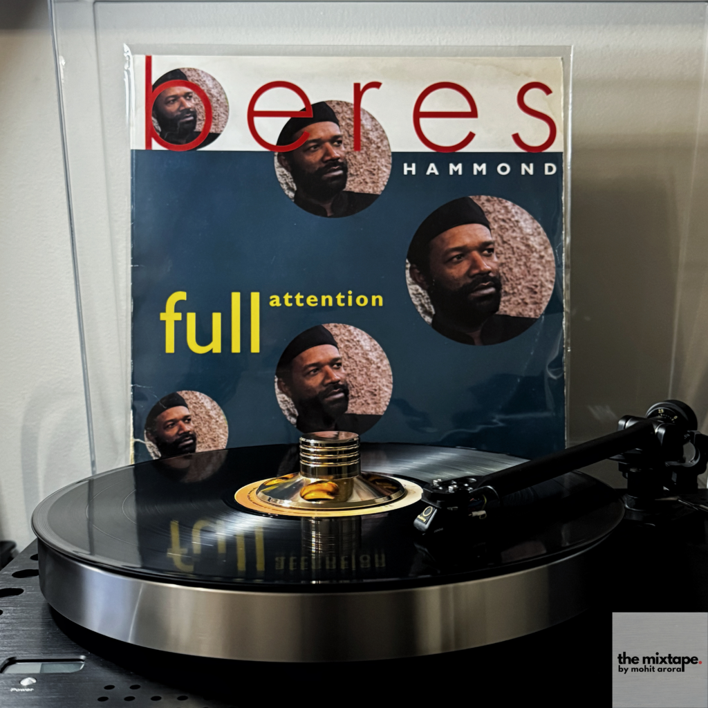 A vinyl record of the album Full Attention by Beres Hammond is displayed on a turntable. The album cover prominently features the title in bold yellow text and the artist's name, "Beres Hammond," in large red and white lettering. The design includes multiple portraits of Beres Hammond, showcasing his thoughtful expression, set against a textured background. The record is actively spinning on a modern turntable with a gold-colored spindle weight